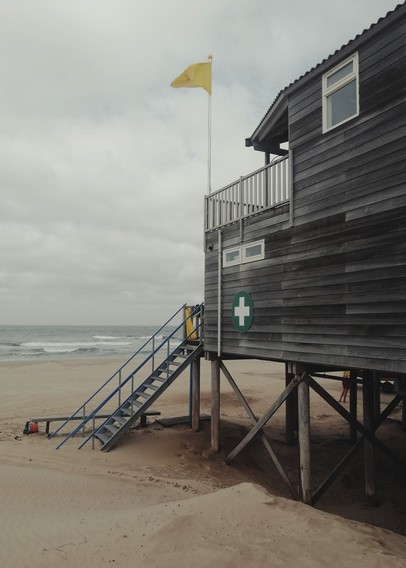 Hölzernes Lifeguard-Häuschen am Strand irgendwo in Holland, irgendwann vor einigen Jahren. Gelbe Fahne weht. Grauer Himmel.
