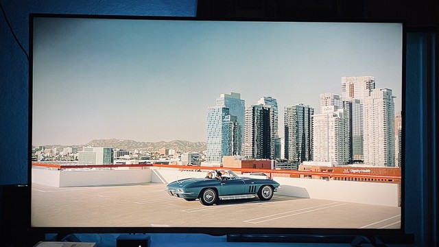A blue convertible car parked on a rooftop parking structure with a city skyline and mountains in the background.