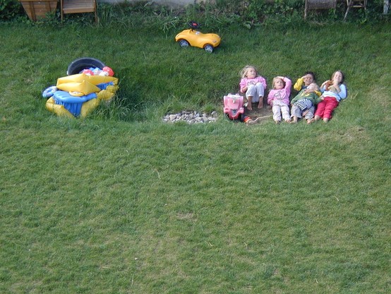 5 Kinder liegen fröhlich auf einer Wiese. Ein paar Spielsachen drum rum. 