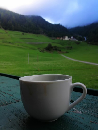 Kaffeetasse vor Bergpanorama. Wolken,  Weiden. 